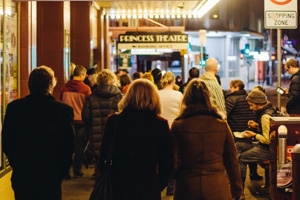 A group of patrons await under the awning lights at the front of the theatre