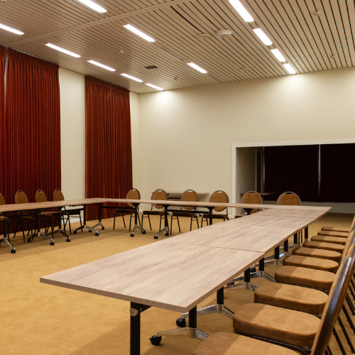 The John Duncan Room set up with long tables and chairs for a meeting or workshop, with red curtains and a built-in stage at the rear.